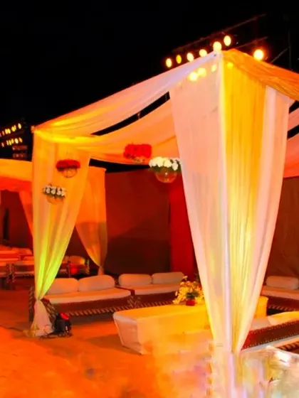 Stylish cabana-style tents with white sofas set up for a sangeet or cocktail night, illuminated with warm orange and yellow lighting.