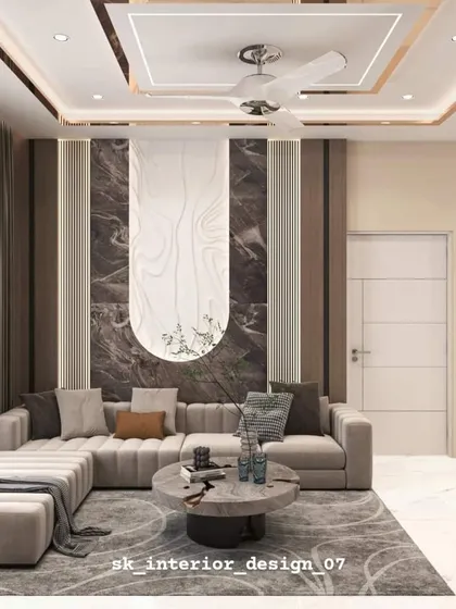 This living room design features a beautiful L-shaped sofa and a statement wall with contrasting marble and wood textures. The false ceiling with cove lighting adds a warm, inviting glow to the entire space.