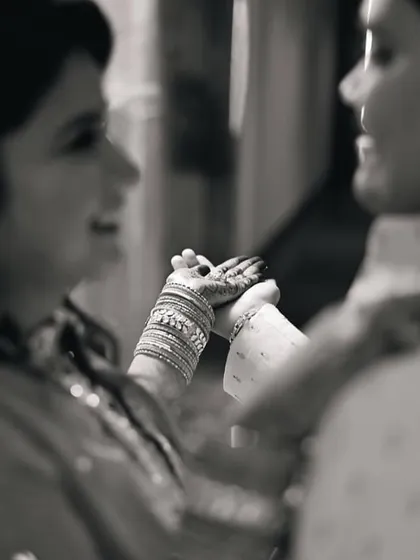 A close-up, black and white photo focusing on the bride's hands, adorned with mehendi and bangles, as she holds the groom's hand. A beautiful detail of connection.