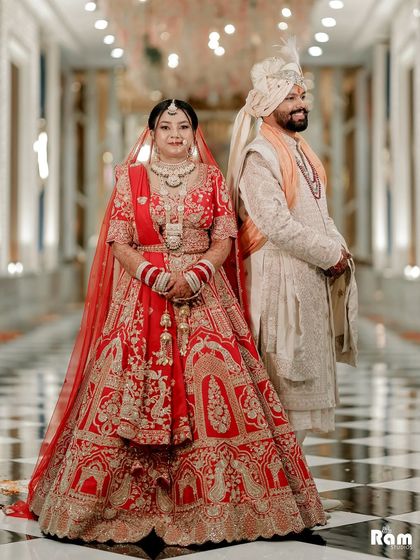 A classic and elegant portrait of the couple in a grand checkered-floor hallway, their red and white outfits creating a striking contrast.