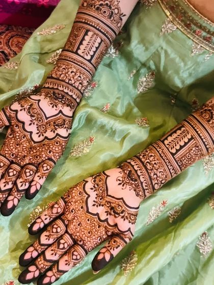 A detailed view of a bridal design against a soft green fabric, showing the contrast and beauty of the henna art.