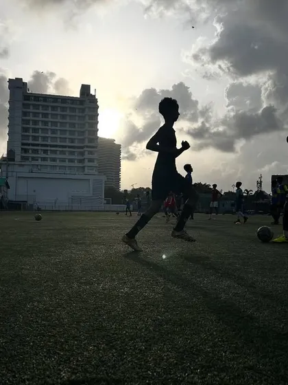 The silhouette of a young player running with the ball against a dramatic sunset sky. This artistic shot captures the beauty and therapeutic nature of the game.