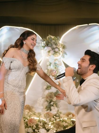 A beautiful moment on stage during the "Big Bow Affair" reception. The groom serenades his bride in front of the statement floral-filled bow backdrop we designed for their special night.