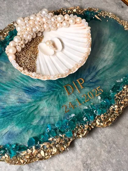 For the couple that loves the sea, I designed this unique ocean-themed ring platter. It features swirling teal and blue resin that mimics ocean waves, a real seashell ring holder adorned with pearls, and a border of sand and crystals. I can personalize it with your initials and special date.