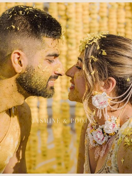 A playful and intimate Haldi moment. The couple, covered in turmeric, touch noses, their smiles radiating pure happiness and love.