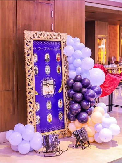 A personalized milestone board for Prince Zeeyan's first year. The photos are displayed within an ornate golden frame, surrounded by a beautiful purple and cream balloon arrangement.