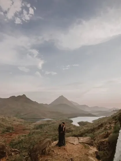 A truly epic pre-wedding photograph featuring a couple overlooking a majestic waterfall and lake. This wide landscape shot showcases our ability to capture love stories in stunning natural locations.