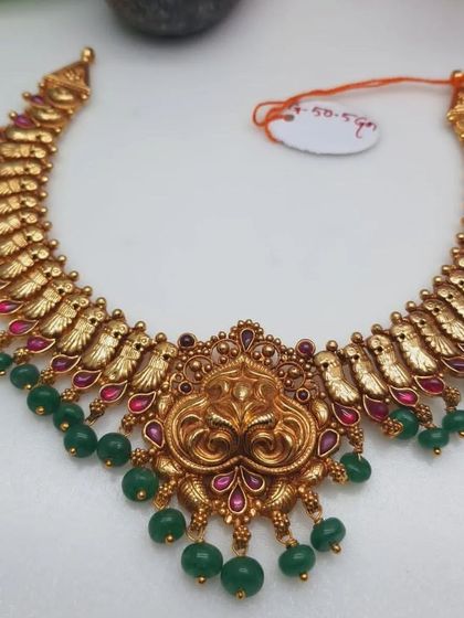 A beautiful temple necklace with a unique design, featuring a lion-faced pendant. The necklace is made from 92.5 silver with gold plating and is finished with green bead drops.