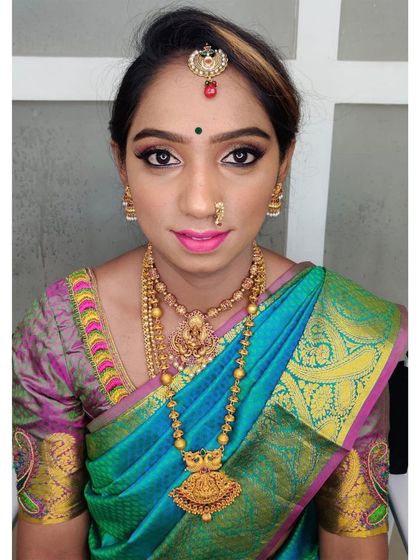 A stunning South Indian bridal look featuring a beautiful turquoise and pink silk saree. The makeup is kept elegant with defined eyes, a bright pink lip, and a natural, glowing complexion.