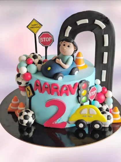 A playful car-themed cake for a 2nd birthday. This design features a road that arches over the cake, traffic signs, and cute fondant cars.