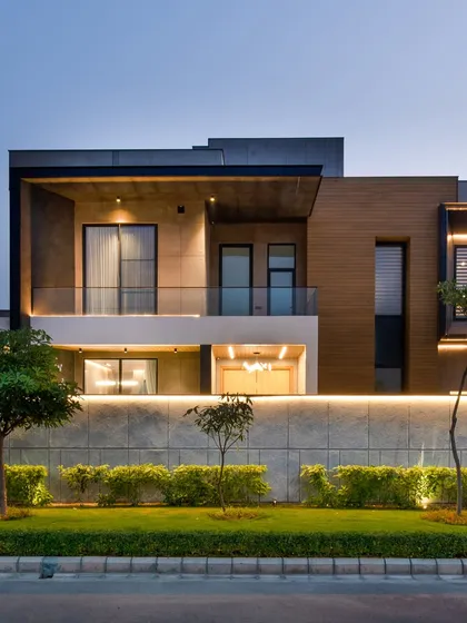 The Sonipat residence at dusk, where landscape lighting highlights the boundary wall and the home's architectural features, creating a warm and inviting atmosphere.