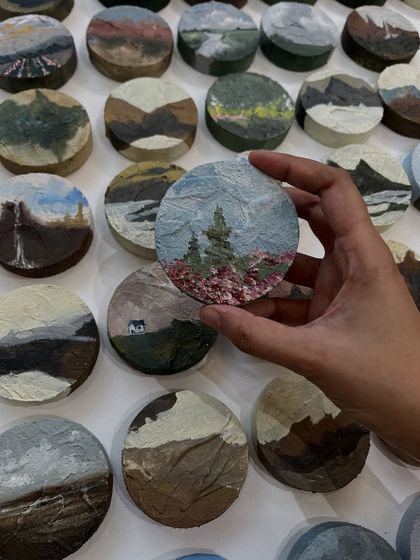 Holding one of the 3-inch nature-inspired miniatures. This one features a mountain scene with pine trees and a field of flowers.