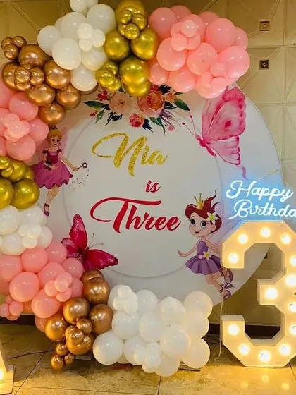 A fairy-themed third birthday party with a custom backdrop and a pink, gold, and white balloon arch.