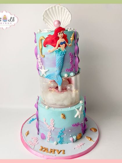 An enchanting two-tiered Little Mermaid cake. This under-the-sea creation features Ariel, shimmering corals, and a separator tier filled with "bubbles."