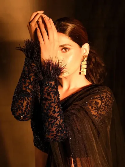 This shot highlights the feathered details of the sleeve and the clean makeup look. The focus remains on the eyes, which are subtly defined to draw the viewer in, even when partially obscured.