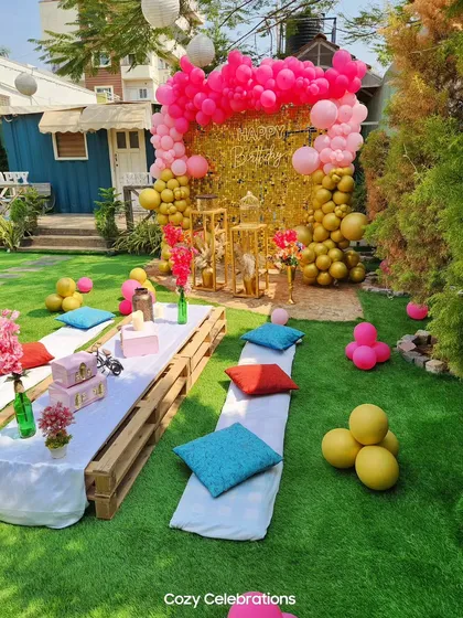 A glamorous take on an outdoor picnic party. This setup features a bright pink and gold color scheme, with a sequin backdrop and a long, low table arrangement for a fun and stylish birthday celebration.