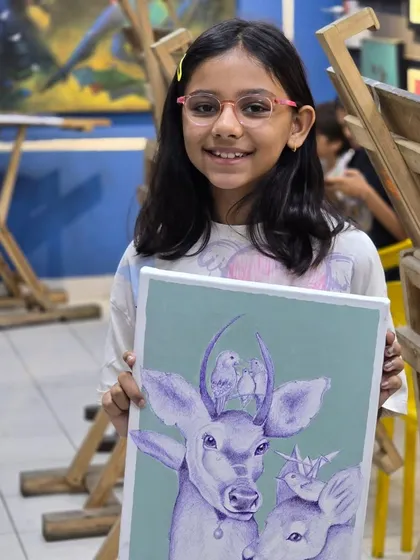A young artist proudly displays her finished ballpoint pen artwork, a whimsical depiction of deer and birds, showcasing her creativity and skill.