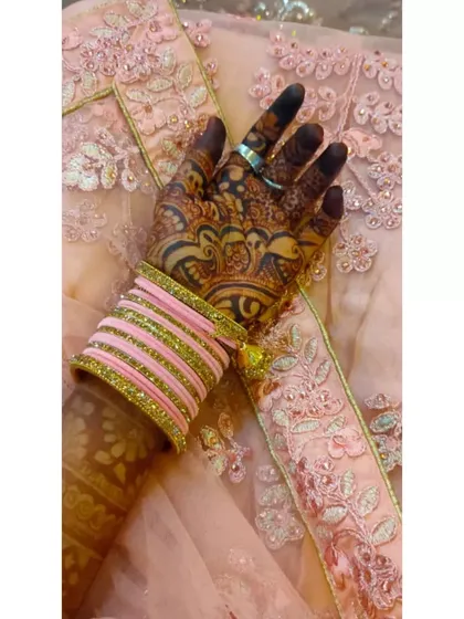 A close-up of a gorgeous, dark peacock feather mehndi stain, paired with pink bridal bangles. The contrast really makes the deep color of the henna pop.