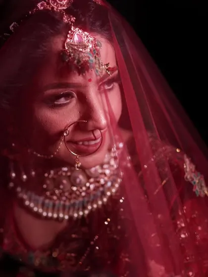 This is the style of bridal portrait I love to create. Using moody, dramatic lighting, I focus entirely on the bride, capturing that quiet moment of anticipation under the red veil. The rich colors of her lehenga and the intricate details of her jewelry, like the nath and maang tikka, stand out beautifully against the dark background.