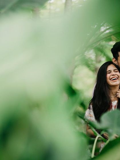 A duplicate of image 21, a candid moment of laughter shared between the couple, framed by vibrant green leaves.