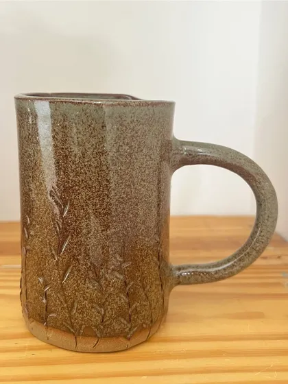 A tall, cylindrical mug with a large, comfortable handle and subtle textured details at the base.