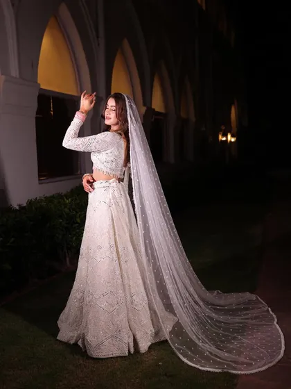 Another angle of the bride in the white lehenga, showing her looking back. The long veil creates a beautiful, ethereal silhouette.