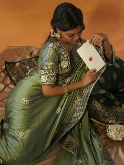 A conceptual shot featuring a model in a lustrous green silk saree, seated and examining a letter with a red wax seal. This image builds a narrative of timeless romance and tradition for the brand.