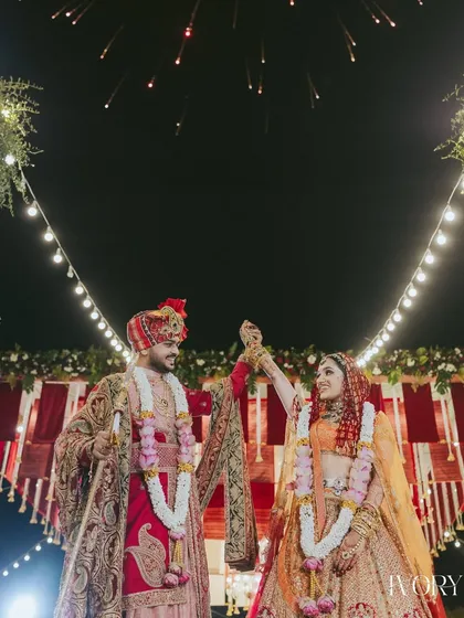 A classic Varmala pose under the stars. The couple's joyful interaction is the centerpiece, framed by festive lights and traditional decor, creating a timeless wedding portrait.