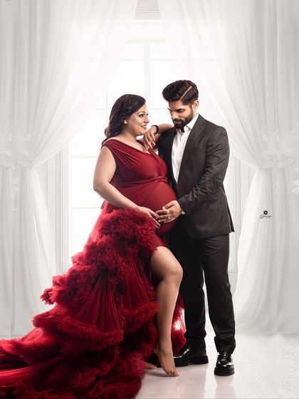A sophisticated couple portrait against a bright window backdrop. The client's dramatic red gown contrasts beautifully with her partner's dark suit, creating a powerful and elegant image.