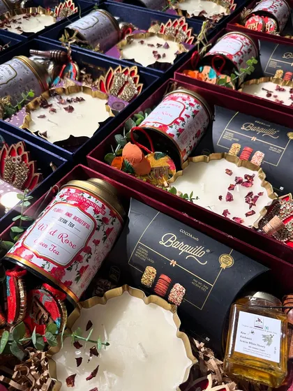 A premium Diwali hamper curated for Aum Papers. This box features artisanal tea, gourmet chocolates, and a hand-poured candle with rose petals, all in a rich, festive color palette.