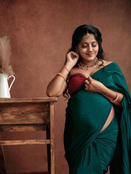 A beautiful, smiling portrait of a mom-to-be in a traditional green saree. The simple props and warm lighting create a classic and elegant look.