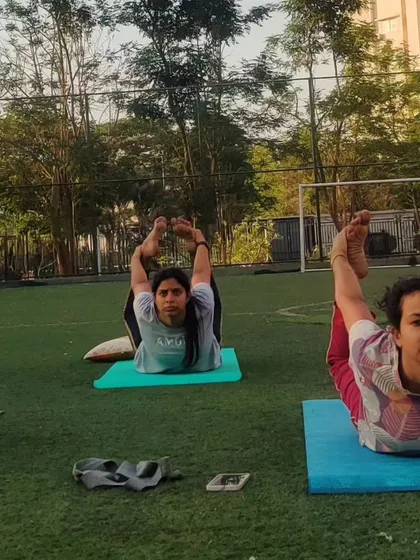 Students in an outdoor class practicing Dhanurasana (Bow Pose). This is a powerful backbend that strengthens the back muscles and opens up the chest and shoulders.