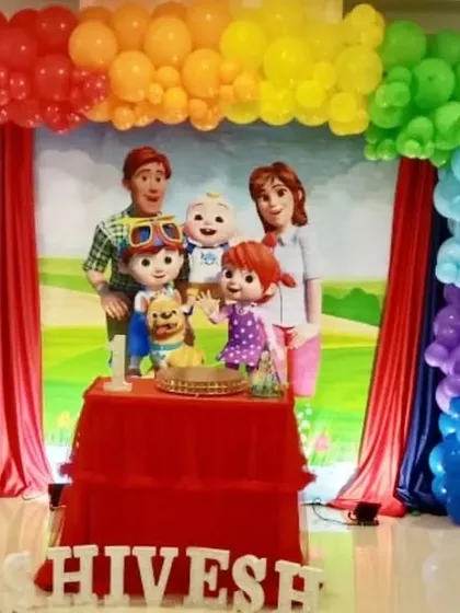 A Cocomelon stage setup with a large character backdrop and a rainbow balloon arch.