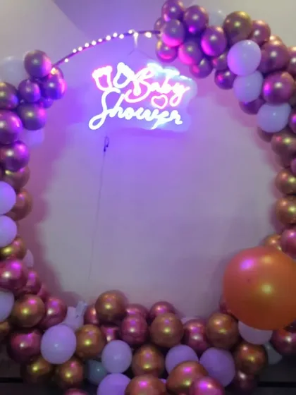 A baby shower ring decoration with a neon sign. The purple, gold, and white chrome balloons create a rich and celebratory look.
