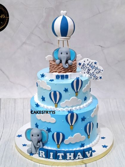 A charming two-tier elephant and hot air balloon cake. This 3kg choco-vanilla cake is decorated in shades of blue with fondant clouds, stars, and a cute elephant topper.
