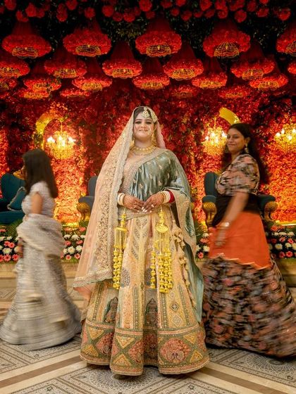 A full-length shot of the bride in her magnificent lehenga, capturing her grand entrance with a sense of motion and energy from the guests around her.