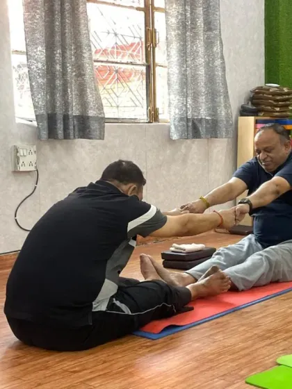 Personal attention is key, especially when working with stiffness. Here, an instructor provides hands-on assistance to a senior client in a seated forward bend, helping him safely deepen the stretch and improve hamstring flexibility.