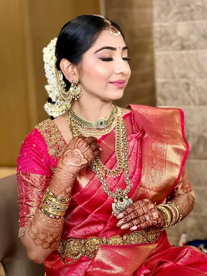 This bride's look is all about traditional elegance. The makeup features golden eyeshadow and a defined lip, complementing her layered gold necklaces and bright pink Kanjivaram saree.