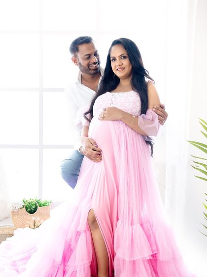 A happy and bright portrait of a couple in a naturally lit studio, with the partner seated behind the mom-to-be.