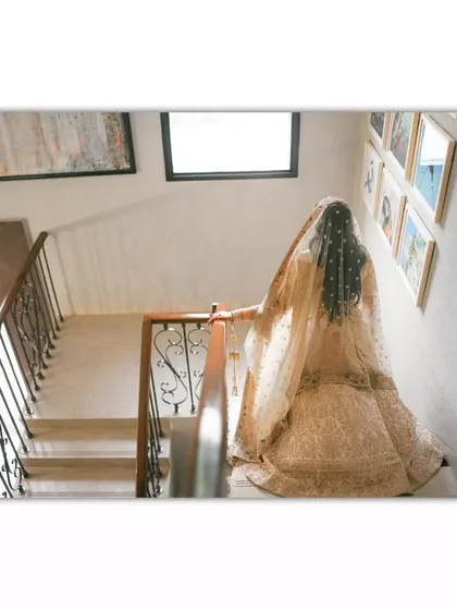 A high-angle shot of the bride descending a staircase, emphasizing the trail of her lehenga.