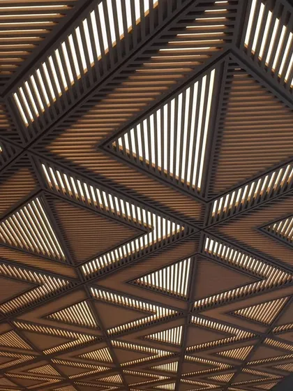 A detailed view of a complex, multi-layered CNC-cut ceiling. The triangular geometric patterns create a visually stunning effect, showcasing the precision and artistic potential of our custom fabrication services.