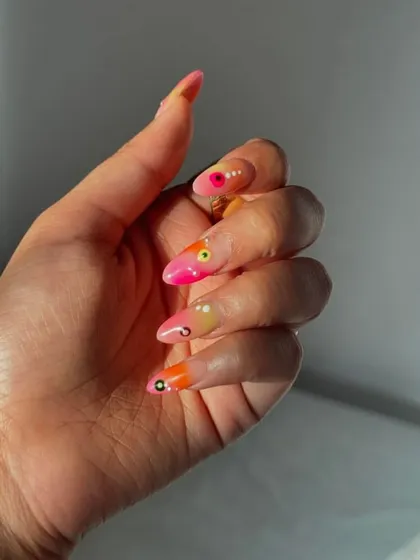 A close-up on the abstract sunset-colored nail art, showing the blend of pinks and oranges with small, detailed dots.