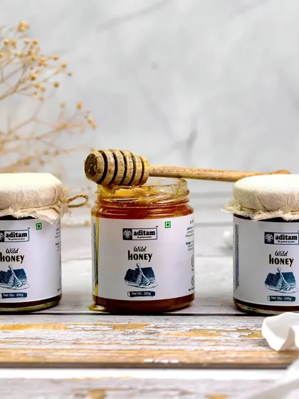 Three jars of wild honey are lined up in a clean, minimalist composition. A honey dipper rests on the open center jar, creating a simple yet inviting image that focuses on the product's natural appeal.