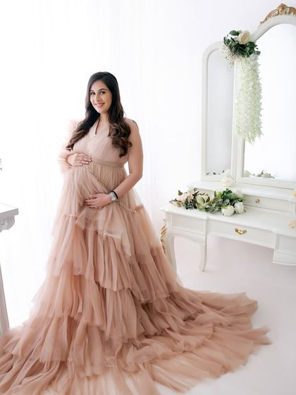 A full-length portrait showcasing the magnificent, cascading ruffles of this beige gown. The mom-to-be looks serene and beautiful in this elegant setup.