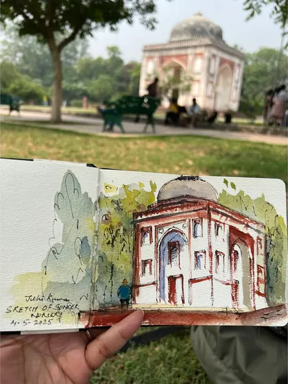 Holding up my finished sketch at Sunder Nursery, with the tomb I painted visible in the distance. This is from a global Urban Sketchers week event.