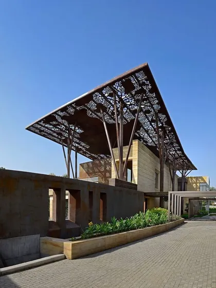 The entrance to the Tree House is framed by a corten steel wall and a paved driveway, leading the eye towards the dramatic structure. The landscaping is designed to complement the architecture's strong lines.