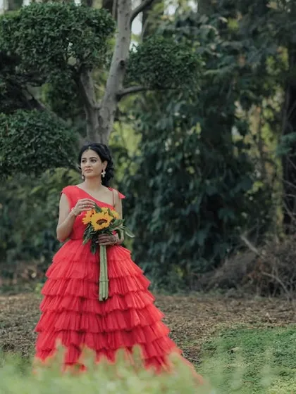 A solo portrait of the bride-to-be in a stunning red gown, holding sunflowers in a forest clearing. This cinematic shot highlights her beauty and the romantic, fairytale-like setting of her Pune pre-wedding shoot.