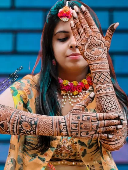 A happy bride showcasing her complete bridal mehandi. This full-arm design includes personalized initials, geometric patterns, and floral bands, all coming together to create a stunning look for her special day.