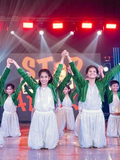 Performers in a concluding pose at a dance show. The lighting is bright and celebratory, with their team name visible on the screen behind them.