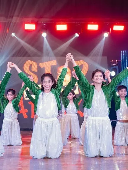 Performers in a concluding pose at a dance show. The lighting is bright and celebratory, with their team name visible on the screen behind them.